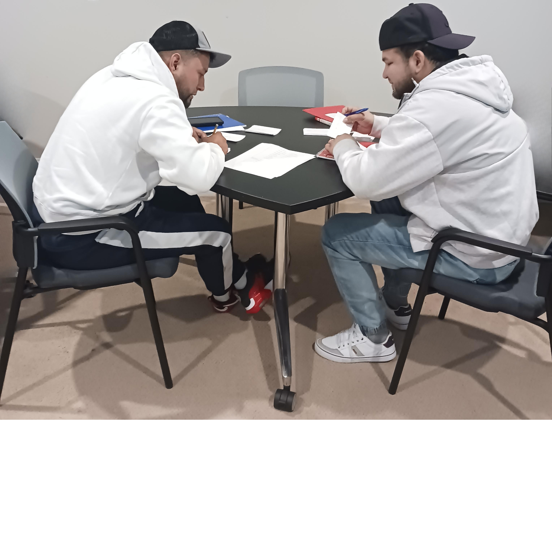 Two adult employees taking notes and studying English at a table during a New Heights Languages class
